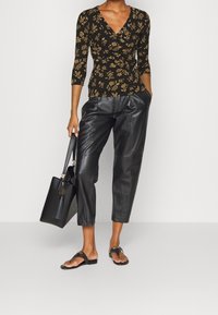 Black floral wrap top with long sleeves, high-waisted black leather trousers, and black flat sandals. Black handbag with tassel detail.
