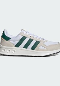 Baskets de sport avec une tige en suède beigne et en maille blanche, des rayures en cuir vert, un col rembourré et une semelle en caoutchouc noir texturé.