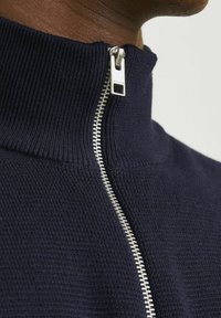 Pulover navy cu fermoar, cu guler înalt, având un fermoar argintiu și un material texturat, aproape, arătând detalii ale materialului și cusăturilor.