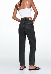 Czarne jeansy z wysokim stanem i prostą nogawką, z delikatnym efektownym blaknięciem i tylnymi kieszeniami. Zestawione z białym krótki topem na ramiączkach i czarnymi sandałami.