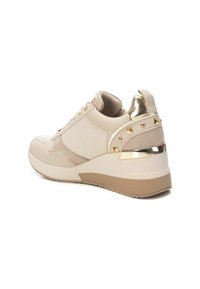Zapatilla beige con parte superior de tela texturizada, detalle metálico en el talón y tachuelas en forma de pirámide. Presenta una suela plataforma gruesa con punta redonda.