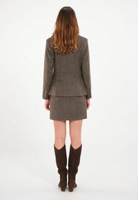 Veste et jupe marron à fines rayures, présentant un design ajusté, un tissu texturé et associées à des bottes en daim marron jusqu'aux genoux.
