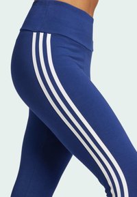 Blå leggings med hög midja, en smidig tygtextur och tre vita vertikala ränder som löper längs sidorna.