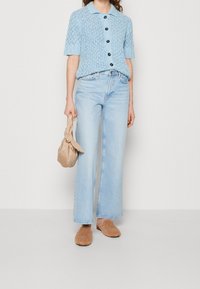 Ljusblå stickad kortärmad topp med krage och svarta knappar, tillsammans med ljusblå vida jeans och bruna fluffiga tofflor.
