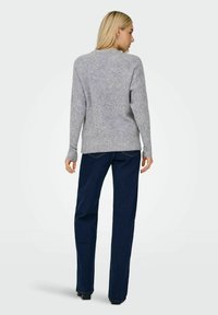 Pull en laine gris à manches longues et texture côtelée, associé à un pantalon droit bleu foncé et des chaussures à talons noires.
