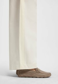 Beige mokkasiner i semsket skinn med en liten dekorativ metallaccent, kombinert med vide, kremfargede bukser med en sidelange stripe.