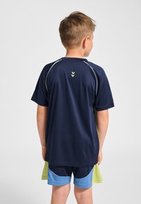 Marinblå sporttröja med korta ärmar, med ljusgröna detaljer och vitt kantband, kombinerad med blå och gröna sportshorts.