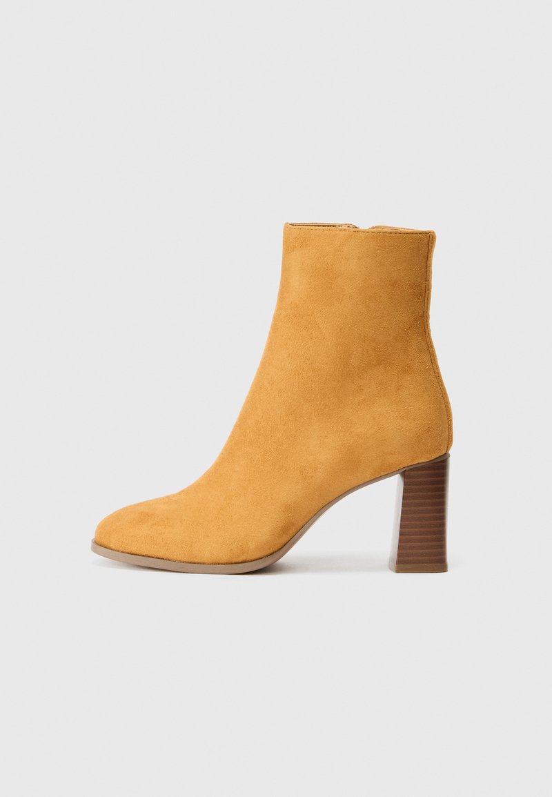 Gelbe Wildleder-Ankle-Boots mit einer runden Zehenpartie, einem strukturierten braunen Blockabsatz und einem glatten Oberdesign. Keine sichtbaren Beschläge oder Verzierungen.
