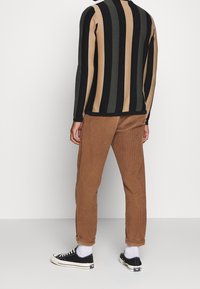 Pull à manches longues rayé en noir, marron et vert olive ; associé à un pantalon en velours côtelé marron et des baskets en toile noire.