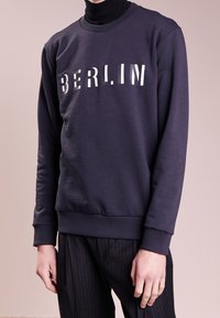 Felpa navy con la scritta "BERLINO" in lettere bianche a contrasto, maniche a costine e scollatura classica, abbinata a pantaloni a righe.
