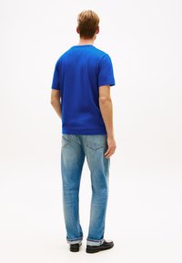 Μπλε κοντομάνικη μπλούζα από βαμβάκι, συνδυασμένη με ανοιχτόχρωμο τζιν. Το πουκάμισο έχει στρογγυλή λαιμόκοψη και κανονική εφαρμογή.