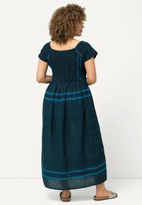 Maksimekko, jossa on lyhyet hihat, musta smokkivartalo ja sininen geometrinen kirjonta tummalla taustalla. Pehmeä kangas, joka laskeutuu kauniisti.