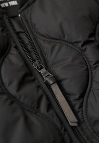 Czarna kurtka puchowa o fakturowanym wykończeniu, z zamkiem błyskawicznym z przodu, czarnym uchwytem oraz widocznymi detalami pikowania.