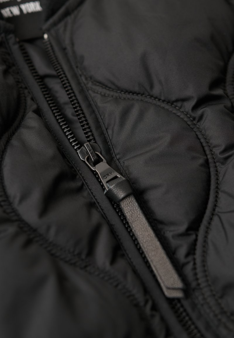 Schwarze Steppjacke mit strukturierter Oberfläche, die einen Frontreißverschluss mit schwarzem Ziehgriff und sichtbarem gestepptem Detail zeigt.