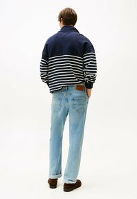 Pullover a righe blu navy e bianche con colletto alto, abbinato a jeans dritti azzurri e scarpe marroni. Vista posteriore dell'outfit.