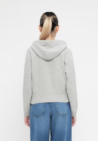 Grauer Kapuzenpullover mit geripptem Saum, strukturierter Stoff und lässiger Passform, kombiniert mit hellblauen Schlagjeans.