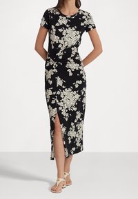 Svart blommig klänning med korta ärmar, som har krämfärgade blommönster, en slit fram och en knuten midjedetalj. Mjukt tyg.