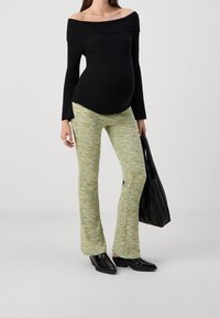 Svart ribbad topp utan axlar kombinerad med gröna mönstrade figurnära byxor och svarta spetstoppar ankelstövlar, bärande en texturerad svart väska.