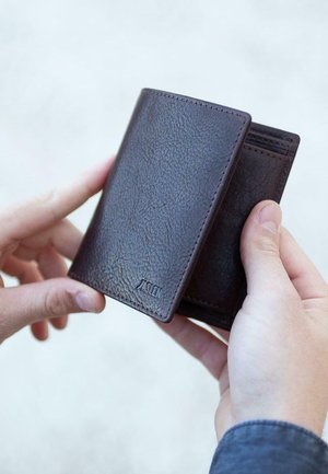 Cartera de cuero marrón oscuro con un acabado texturizado, que cuenta con múltiples ranuras para tarjetas y una marca en relieve, sostenida entre dos manos.