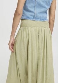 Jupe verte olive à taille smockée avec un tissu fluide, une texture subtile et un drapé doux, associée à un crop top en denim clair.