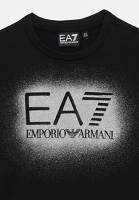 Mustast puuvillast T-särk, millel on hõbedast toonidega gradientgraafika ja "EA7" ning "EMPORIO ARMANI" logod. Ümara kaelusega, lühikeste varrukatega.