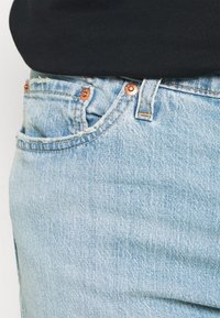 Pantalones vaqueros de mezclilla de color azul claro con un diseño clásico de cinco bolsillos, herrajes de cobre y detalles de costura visibles a lo largo de la cintura.