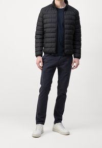 Czarna kurtka puchowa z poziomym pikowaniem, zamek z przodu i stójka. Ciemnoniebieskie spodnie i białe sneakersy dopełniają outfit.