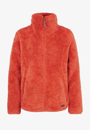 Fleece jack in feloranje, hoge kraag, met rits aan de voorkant. In combinatie met blauwe skibroeken en bruine laarzen van waterdicht materiaal.