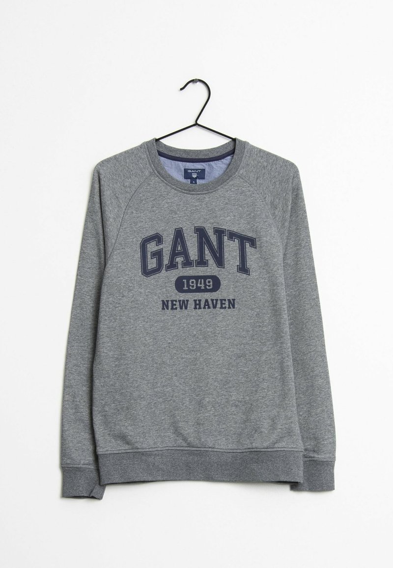 Sweat-shirt gris à manches longues et col rond avec l'inscription « GANT 1949 New Haven » imprimée en bleu marine, suspendu à un cintre noir sur un fond blanc.