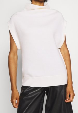 Top senza maniche di maglia rosa chiaro con colletto alto, texture morbida e orlo a coste, abbinato a pantaloni in pelle nera.