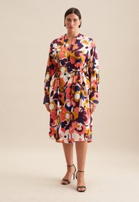Farbenfrohes Blumendruckkleid mit langen Ärmeln, Taillengurt, knielangem Saum und glattem Stoff. Schwarze Riemchenabsätze.