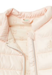 Světlý růžový prošívaný kabát se stříbrným zipem, límcem a vnitřním podšíváním s opakujícím se vzorem králičí hlavy v jemné broskvové barvě.