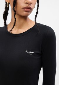 Melnas garās piedurknes krekls, izgatavots no mīksta auduma. Tam ir apaļa kakla izgriezuma forma un neliels balts "Pepe Jeans London" logo uz krūtīm.