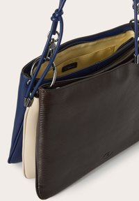 Bolso de tres compartimentos en marrón oscuro, crema y azul marino. Presenta cuero texturizado y acentos lisos, con una correa desmontable y cierres con cremallera.