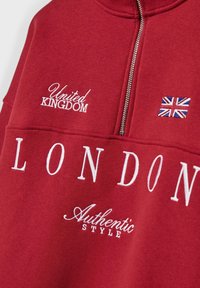 Felpa rossa con mezza cerniera, ricamo bianco con le scritte "LONDON", "United Kingdom" e "Authentic Style", con una piccola toppa della Union Jack.