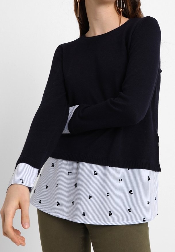 Mörkblå långärmad tröja lager på lager över en ljusblå och vit randig skjorta med små svarta tryckdetaljer. Mjuk stickad kvalitet.