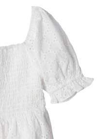 Vit klänning med ett strukturerat mönster, smockad bodice och pösiga ärmar, accentuerad med volanger vid ärmsluten. Lättvikts bomullstyg.