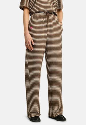 Pantalones de pierna ancha con rayas marrones y blancas, cintura con cordón, usados con zapatos negros y un pequeño detalle de corazón rosa en el muslo izquierdo.