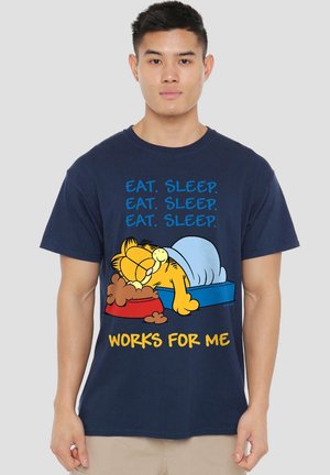 Man wearing navy shirt with Garfield sleeping in bed next to food bowl, text "Eat. Sleep. Eat. Sleep. Eat. Sleep. Works for me."