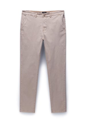 Beige chinot valmistettu puuvillasta, jossa on nappisuljenta, viisi taskua ja kapenevat lahkeet, sekä ompeluyksityiskohdat saumoissa.