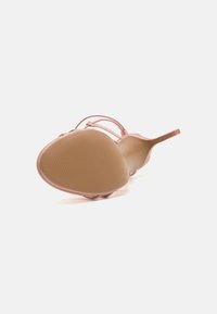 Vaaleanpunaiset korkokengät, joissa on ohuet hihnat, terävä kärki ja ribattu beige kumipohja. Yläosan materiaali on sileää ja kiiltävää.