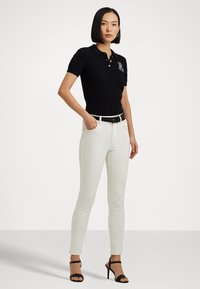 Polo en tricot marine avec motif en cable, manches courtes et logo. Associé à un jean skinny blanc et des talons noirs à lanières ; design épuré.