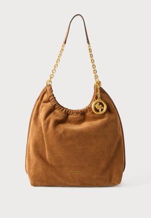 Sac à bandoulière en daim marron avec chaîne dorée et pendentif rond en or du logo Michael Kors suspendu près du haut.