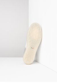Semelle de chaussure en matériau caoutchouteux blanc texturé, dotée d'un accent argenté, d'un logo circulaire et d'un design de lignes entrecroisées pour une meilleure traction.