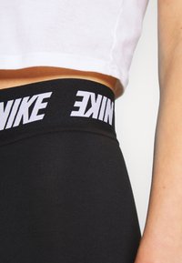 Black leggings with a wide, elastic waistband featuring white "NIKE" logo. The fabric appears smooth and stretchy, ideal for active wear.