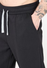 Zwarte joggingsbroek van zachte stof, met een elastische tailleband, grijze trekkoord en zijzakken voor extra gemak.
