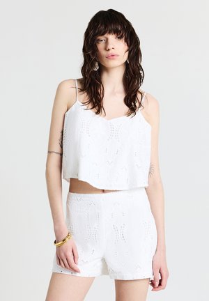 Set di top corto bianco e pantaloni corti con motivi floreali ricamati e dettagli a taglio. Tessuto leggero e spalline regolabili.