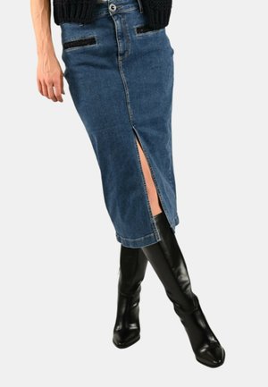 Gonna a tubino in denim con spacco frontale, di colore blu scuro, due tasche e dettagli cuciti. Indossata con stivali neri in pelle al ginocchio.