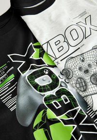 Two T-shirts: one black with a green gaming controller graphic, the other white with black "XBOX" text and a controller outline.