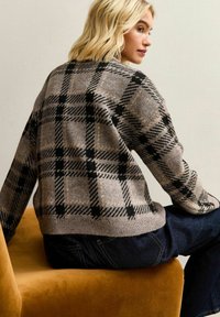 Maglione a quadri beige e nero realizzato in morbido tessuto a maglia, con maniche lunghe, scollatura rotonda e un fit leggermente corto e accogliente.